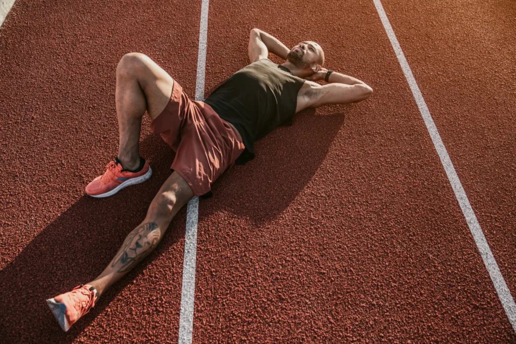 Runner lying on a red running track, resting after a workout