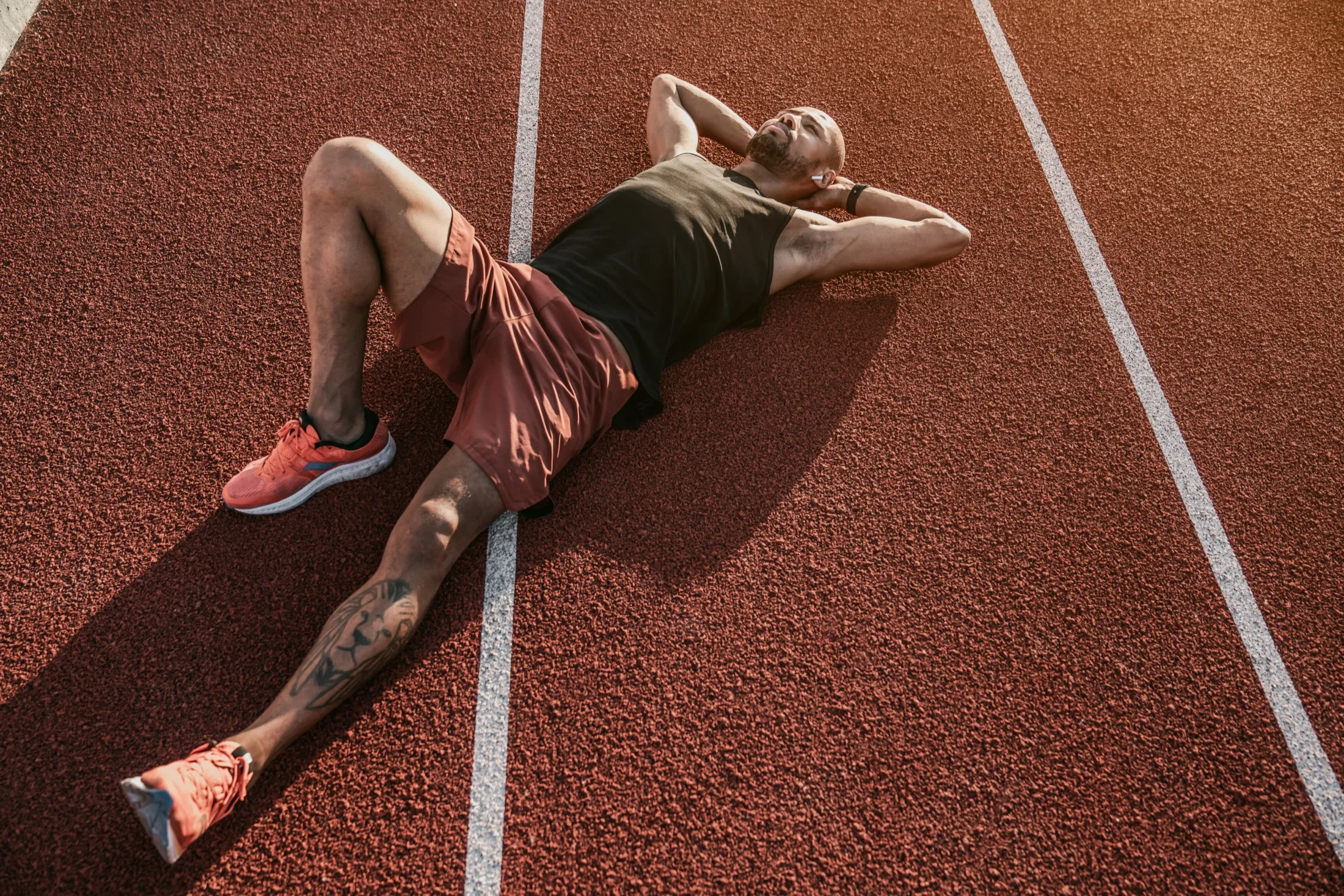 Runner lying on a red running track, resting after a workout